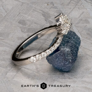 The Pave "Vilaine" band in 14K white gold, set with marquise-cut diamonds, rests on rough blue-green mineral atop a textured gray surface, displayed above the “EARTH’S TREASURY” logo.