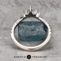The Pave "Vilaine" band in 14K white gold, set with marquise-cut diamonds, rests on rough blue-green mineral atop a textured gray surface, displayed above the “EARTH’S TREASURY” logo.