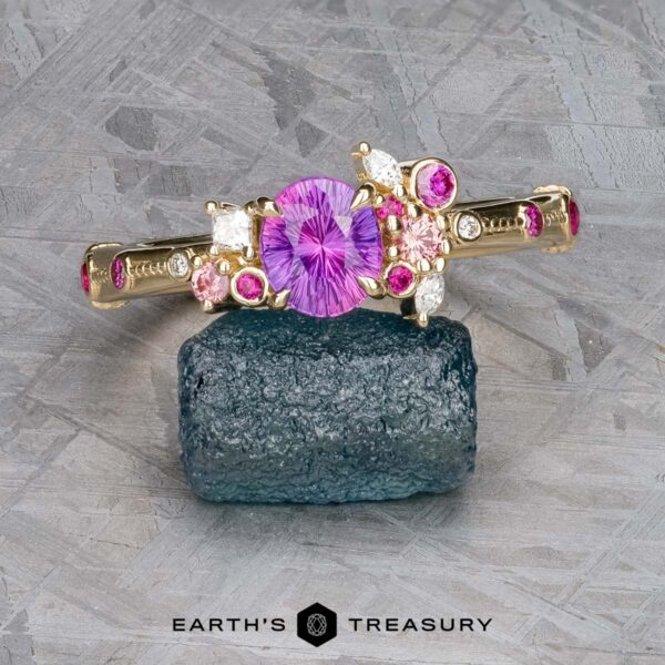 The Linnea ring in 14K yellow gold with 1.15-carat Ceylon sapphire The Linnea ring in 14K yellow gold features a 1.15-carat Ceylon sapphire center, surrounded by pink and white accent stones, displayed on a rough dark blue crystal with the "EARTH'S TREASURY" logo below.