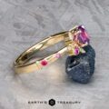 The Linnea ring in 14K yellow gold with a 1.15-carat Ceylon sapphire is shown leaning on a rough dark stone atop a textured gray surface, with the "Earth's Treasury" logo visible at the bottom.