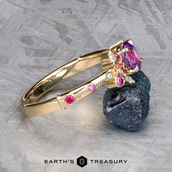 The Linnea ring in 14K yellow gold with 1.15-carat Ceylon sapphire The Linnea ring in 14K yellow gold with a 1.15-carat Ceylon sapphire is shown leaning on a rough dark stone atop a textured gray surface, with the "Earth's Treasury" logo visible at the bottom.