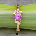 The Linnea ring in 14K yellow gold features a 1.15-carat round Ceylon sapphire centerpiece, accented by pink and white stones, displayed on a green leaf with the Earth's Treasury logo below.