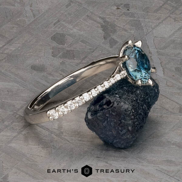 The Pave "Elenin" ring in platinum with 1.21-carat Montana sapphire The Pave "Elenin" ring in platinum, featuring a 1.21-carat Montana sapphire and pavé diamonds on the band, is displayed on a dark stone with a textured gray background.