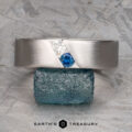 The "Parnis" ring in 14k brushed white gold features a white and a blue gemstone set diagonally, shown atop a rough blue-green crystal.