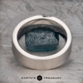A brushed 14k white gold "Parnis" ring encircles a rough blue gemstone, set on a textured gray surface with the text "EARTH'S TREASURY" below.