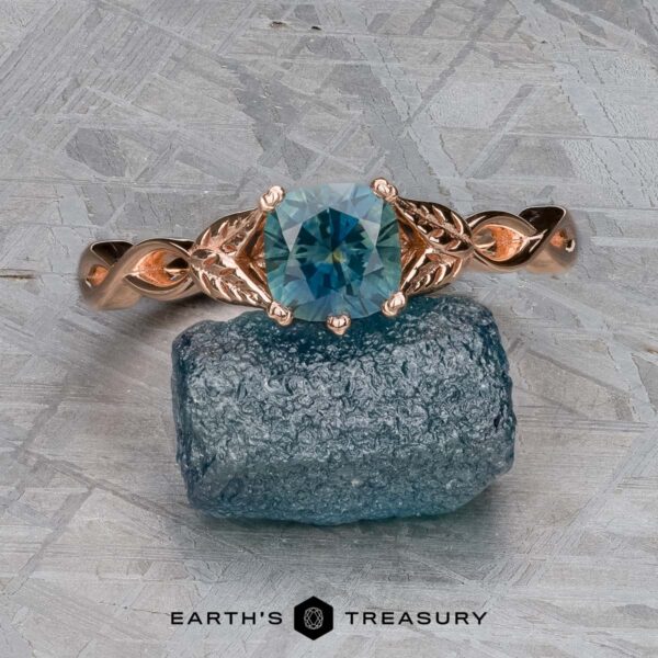 The "Kirryn" ring in 14k rose gold with 1.07-carat Montana sapphire The "Kirryn" ring in 14k rose gold with a 1.07-carat Montana sapphire is displayed on a rough blue stone atop a textured gray background, with the Earth's Treasury logo visible below.