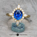 The "Francoise" ring in 18k yellow gold, featuring a 2.28-carat oval Ceylon sapphire surrounded by clear stones, is displayed on a rough blue mineral with the "Earth's Treasury" logo below.