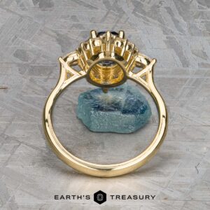 The "Francoise" ring in 18k yellow gold with a 2.28-carat Ceylon sapphire stands upright on a blue-green raw gemstone, with "Earth's Treasury" branding below.