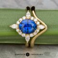 The "Francoise" ring in 18k yellow gold features a 2.28-carat Ceylon sapphire, accented by round and marquise white stones, with its custom-fit contour band, shown on a green background with the "Earth’s Treasury" logo.