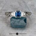 A platinum "Pallas" ring featuring a 0.73-carat Montana sapphire is displayed upright on a rough blue stone, set against a textured gray background.