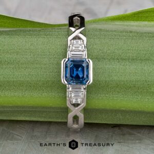 The "Pallas" platinum ring with a 0.73-carat Montana sapphire and sparkling side stones is displayed on a green leaf, with the Earth's Treasury logo at the bottom.
