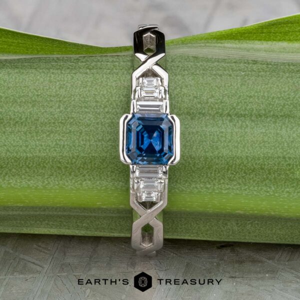 The "Pallas" ring in platinum with 0.73-carat Montana sapphire The "Pallas" platinum ring with a 0.73-carat Montana sapphire and sparkling side stones is displayed on a green leaf, with the Earth's Treasury logo at the bottom.