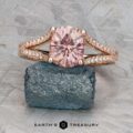 The "Senna" ring in 14k rose gold, featuring a 2.20-carat round Umba sapphire and diamond accents, is displayed on a rough blue-green stone against a textured gray background.