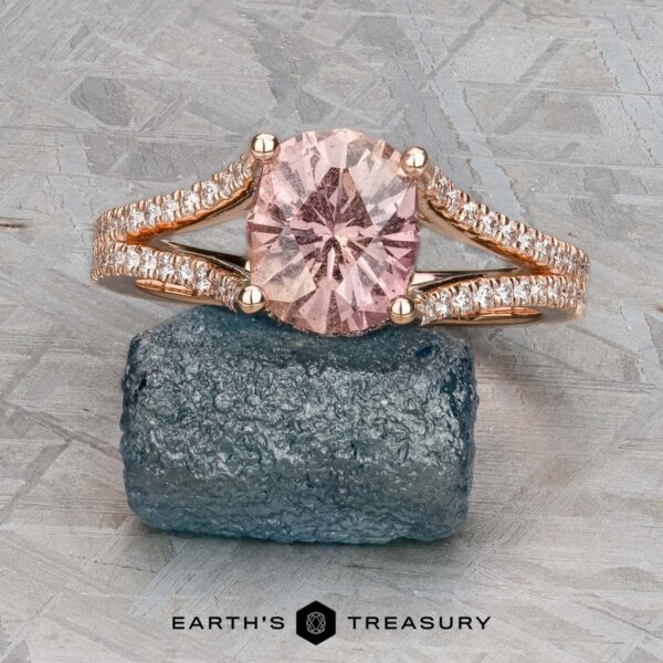 The "Senna" ring in 14k rose gold with 2.20-carat Umba sapphire The "Senna" ring in 14k rose gold, featuring a 2.20-carat round Umba sapphire and diamond accents, is displayed on a rough blue-green stone against a textured gray background.