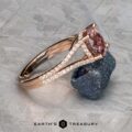 The "Senna" ring in 14k rose gold, featuring a 2.20-carat pink Umba sapphire and diamond accents, is displayed leaning on a rough gray stone with the Earth's Treasury logo at the bottom.