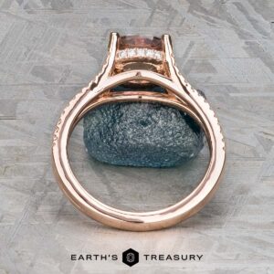 The "Senna" ring in 14k rose gold, featuring a 2.20-carat rectangular Umba sapphire and small diamonds, is displayed upright on a rough gray stone with the Earth's Treasury logo below.