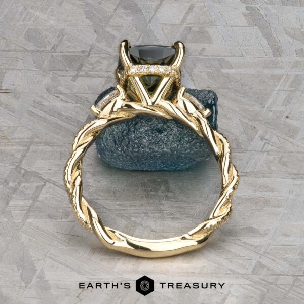 The "Lenore" ring in 14k yellow gold with 2.51-carat Australian sapphire The "Lenore" ring in 14k yellow gold features a twisted, vine-like band and a 2.51-carat Australian sapphire, shown upright on textured stone. "EARTH'S TREASURY" appears at the bottom.