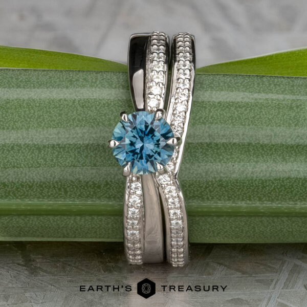 The "Astrid" ring in platinum with 0.98-carat Montana sapphire, alongside the "Faye" band in platinum The "Astrid" ring in platinum with a 0.98-carat Montana sapphire, shown with the "Faye" platinum band, is displayed on a green leaf with the Earth’s Treasury logo below.
