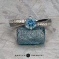 The "Astrid" ring in platinum, featuring a 0.98-carat round Montana sapphire and accent diamonds, is shown on a rough blue stone with the "Earth's Treasury" logo beneath.