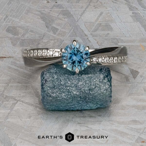 The "Astrid" ring in platinum with 0.98-carat Montana sapphire The "Astrid" ring in platinum, featuring a 0.98-carat round Montana sapphire and accent diamonds, is shown on a rough blue stone with the "Earth's Treasury" logo beneath.