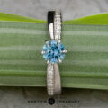 The "Astrid" ring in platinum features a 0.98-carat Montana sapphire and small clear accent stones, displayed on a green leaf with "Earth's Treasury" branding below.