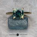 The Cathedral "Begonia" ring in 14k yellow gold with a 2.27-carat Australian sapphire is displayed on a rough blue-green mineral, with the "EARTH'S TREASURY" logo at the bottom.