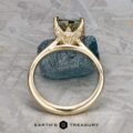 The Cathedral "Begonia" ring in 14k yellow gold, featuring a 2.27-carat Australian sapphire, is displayed upright before a rough stone. The "EARTH'S TREASURY" logo appears at the bottom.