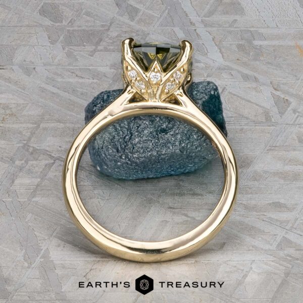 The Cathedral "Begonia" ring in 14k yellow gold with 2.27-carat Australian sapphire The Cathedral "Begonia" ring in 14k yellow gold, featuring a 2.27-carat Australian sapphire, is displayed upright before a rough stone. The "EARTH'S TREASURY" logo appears at the bottom.