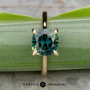 The Cathedral "Begonia" ring in 14k yellow gold with a 2.27-carat Australian sapphire is displayed upright on a green leaf. The text "Earth's Treasury" appears at the bottom.