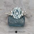 The Comet ring in platinum, featuring a 3.53-carat round Montana sapphire and side diamonds, is displayed on a rough blue gemstone atop a gray textured surface.