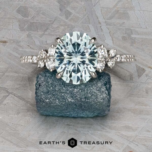 The Comet ring in platinum with 3.53-carat Montana sapphire The Comet ring in platinum, featuring a 3.53-carat round Montana sapphire and side diamonds, is displayed on a rough blue gemstone atop a gray textured surface.