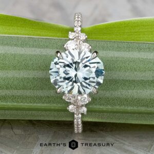 The Comet ring in platinum, featuring a 3.53-carat Montana sapphire and diamonds on the band, is displayed on a green striped leaf. "Earth's Treasury" appears at the bottom.