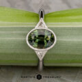 The "Ceres" ring in 14K white gold features a 2.52-carat Madagascar sapphire accented by two triangular clear stones, displayed on a light green plant stem.