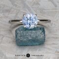 The "Tiara" ring in platinum with a 2.00-carat Montana sapphire is displayed on a rough blue gemstone, set against a textured gray background with the Earth’s Treasury logo at the bottom.