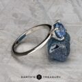 The "Tiara" ring in platinum, set with a 2.00-carat Montana sapphire, rests on a rough blue stone atop a textured gray surface. The "Earth's Treasury" logo is shown at the bottom.