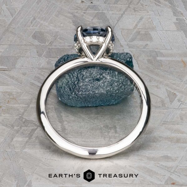 The "Tiara" ring in platinum with 2.00-carat Montana sapphire The "Tiara" ring in platinum features a 2.00-carat Montana sapphire accented by small clear stones, displayed upright on a textured gray stone, with the "Earth's Treasury" logo at the bottom.