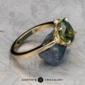 The "Marisol" ring in 14k yellow gold, featuring a 2.90-carat Australian sapphire, is displayed leaning on a rough blue mineral against a textured gray background. The "EARTH'S TREASURY" logo appears at the bottom.