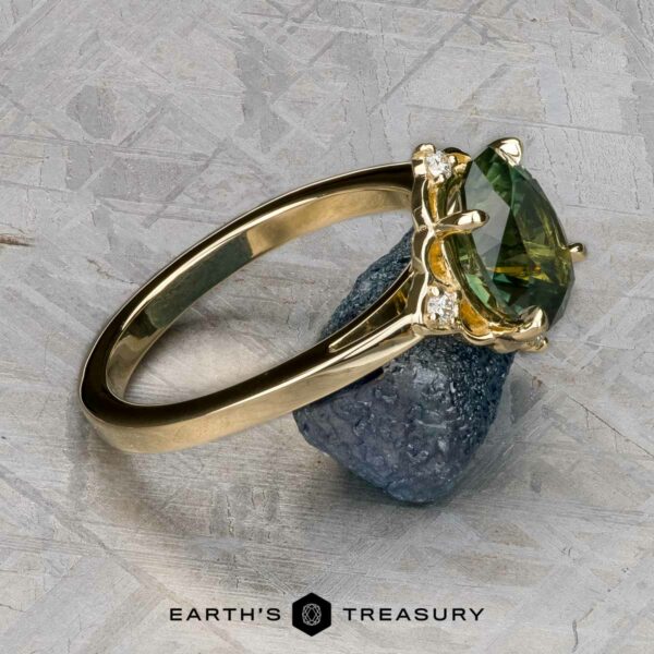 The "Marisol" ring in 14k yellow gold with 2.90-carat Australian sapphire The "Marisol" ring in 14k yellow gold, featuring a 2.90-carat Australian sapphire, is displayed leaning on a rough blue mineral against a textured gray background. The "EARTH'S TREASURY" logo appears at the bottom.