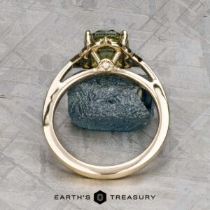 The "Marisol" ring in 14k yellow gold with a 2.90-carat Australian sapphire stands upright on a rough stone surface, featuring the Earth's Treasury logo at the bottom.