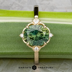 The "Marisol" ring in 14k yellow gold, featuring a 2.90-carat Australian sapphire and accent diamonds, is displayed on a green stem with the "Earth's Treasury" logo below.