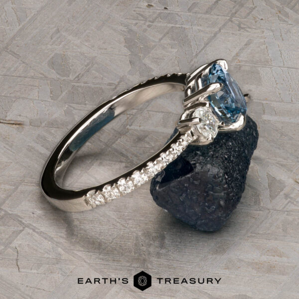 The Pave "Dryope" ring in platinum with 1.15-carat Montana sapphire A platinum Pave "Dryope" ring with a 1.15-carat Montana sapphire and small diamonds rests on rough dark stone. "Earth's Treasury" is shown at the bottom.