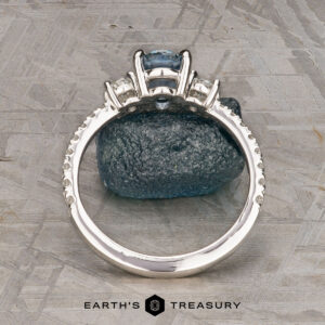 The Pave "Dryope" ring in platinum features a 1.15-carat Montana sapphire centerpiece and side stones, displayed upright on a rough blue mineral with the Earth's Treasury logo below.