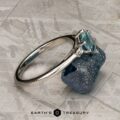 The "Bridget" ring in platinum, featuring a 1.20-carat Montana sapphire, is shown resting on a rough blue mineral against a geometric patterned background.