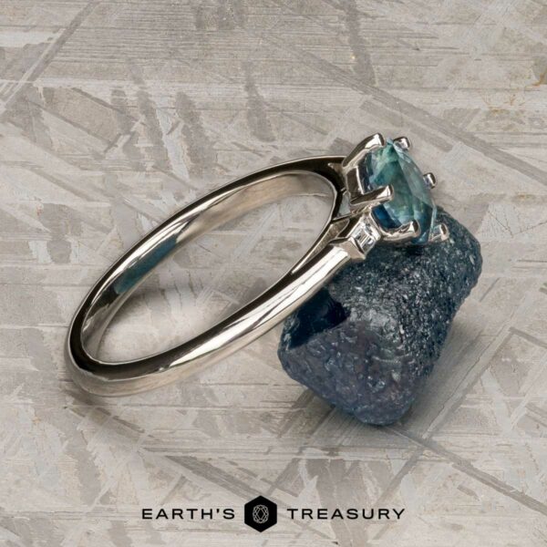 The "Bridget" ring in platinum with 1.20-carat Montana sapphire The "Bridget" ring in platinum, featuring a 1.20-carat Montana sapphire, is shown resting on a rough blue mineral against a geometric patterned background.
