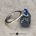The Cathedral "Alyssum" ring in platinum with a 1.83-carat Ceylon sapphire rests on a rough blue stone, set against a gray textured background featuring the Earth's Treasury logo at the bottom.