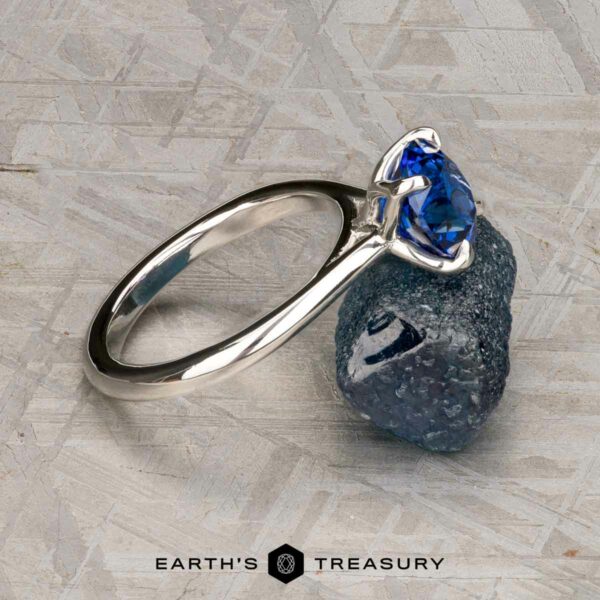 The Cathedral "Alyssum" ring in platinum with 1.83-carat Ceylon sapphire The Cathedral "Alyssum" ring in platinum with a 1.83-carat Ceylon sapphire rests on a rough blue stone, set against a gray textured background featuring the Earth's Treasury logo at the bottom.
