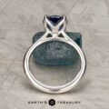 A platinum Cathedral "Alyssum" ring with a 1.83-carat Ceylon sapphire stands upright on a textured gray surface, exuding elegance. The "Earth's Treasury" logo appears at the bottom.