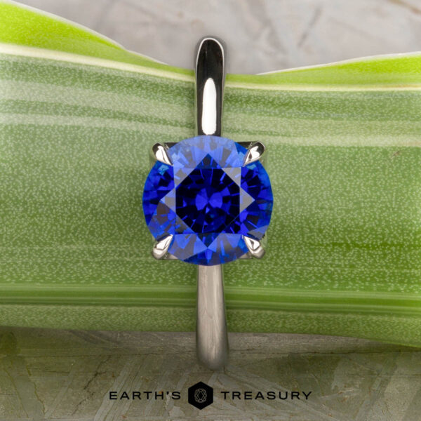 The Cathedral "Alyssum" ring in platinum with 1.83-carat Ceylon sapphire A platinum Cathedral "Alyssum" ring featuring a 1.83-carat Ceylon sapphire is displayed upright against a green leaf background. The "Earth's Treasury" logo appears at the bottom.