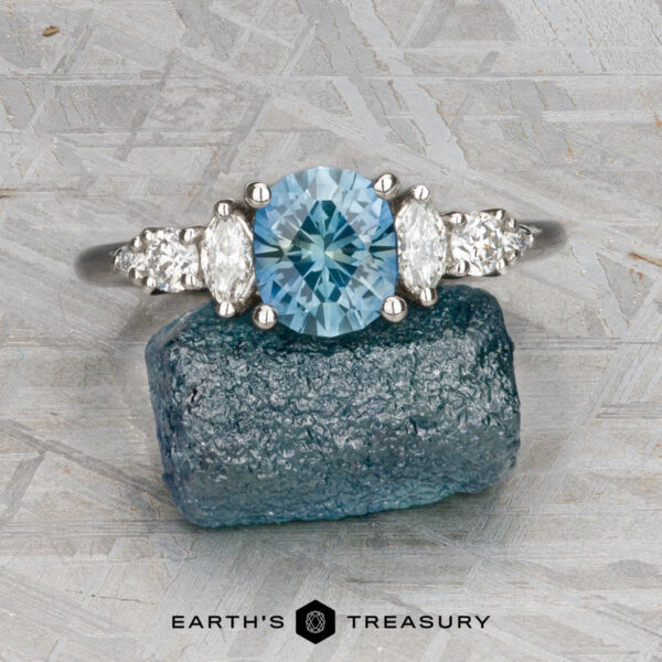 The "Tigrina" ring in platinum with 1.25-carat Montana sapphire The "Tigrina" ring in platinum, featuring a 1.25-carat Montana sapphire and diamond accents, is displayed on a rough blue stone with a textured gray background and the “Earth’s Treasury” logo at the bottom.