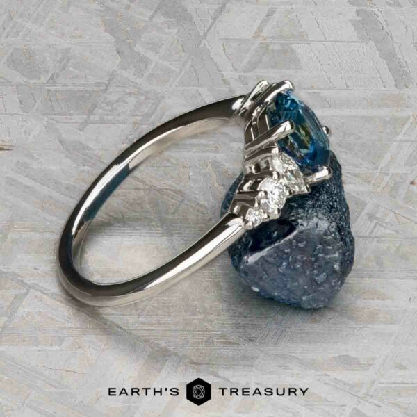 The "Tigrina" ring in platinum with 1.25-carat Montana sapphire The "Tigrina" ring in platinum, featuring a 1.25-carat Montana sapphire and accent diamonds, rests on a textured blue mineral; “EARTH'S TREASURY” appears underneath.